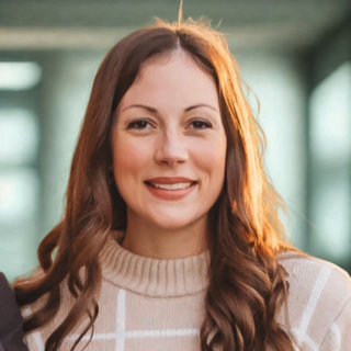 A woman with long, brown hair smiling warmly, wearing a beige sweater with a grid pattern.